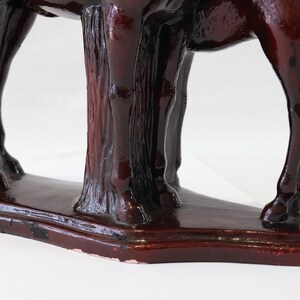 May include: A dark red ceramic horse figurine with a detailed sculpted mane and tail. The horse is standing on a base with a textured surface.