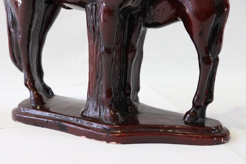 May include: A dark red ceramic horse figurine with a detailed sculpted mane and tail. The horse is standing on a base with a textured surface.