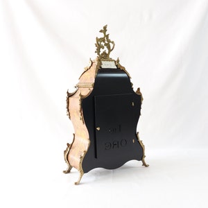 May include: A black and gold clock with intricate carvings and a decorative top. The clock has a black face with a white inscription that reads "ORE 12".