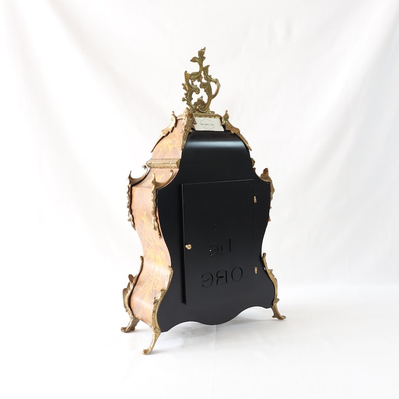 May include: A black and gold clock with intricate carvings and a decorative top. The clock has a black face with a white inscription that reads "ORE 12".