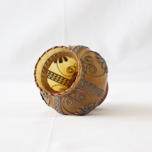 May include: A brown glass vase with a silver wire design. The vase is decorated with a floral pattern and has a scalloped rim.