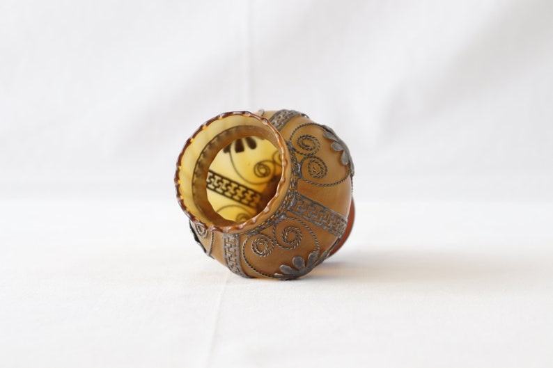 May include: A brown glass vase with a silver wire design. The vase is decorated with a floral pattern and has a scalloped rim.