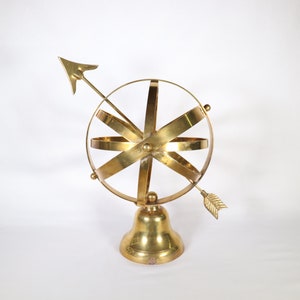 May include: A gold-colored metal sculpture of a sphere with a compass arrow pointing to the right. The sphere is on a bell-shaped base.