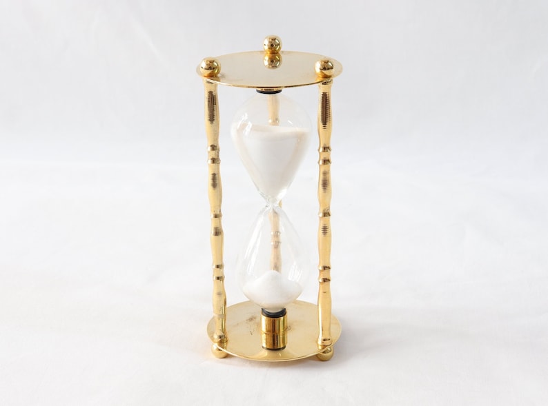 Pu&ograve; includere: Una clessidra color oro con un centro in vetro trasparente riempito di sabbia bianca. La clessidra ha un design decorativo e ornato con una base e una parte superiore rotonde ed &egrave; sostenuta da quattro montanti color oro.