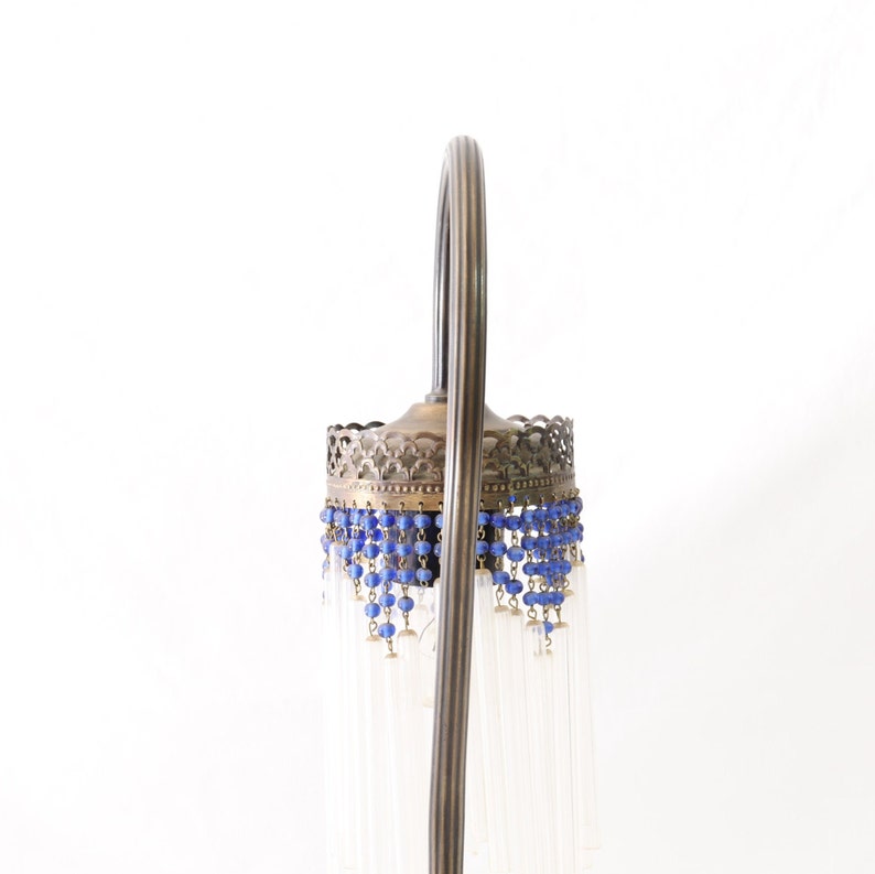 K&ouml;nnte beinhalten: Eine Vintage-Stehlampe mit einem Messingfu&szlig; und einem wei&szlig;en Glasschirm. Der Schirm ist mit blauen Perlen und klaren Glasf&auml;den verziert.