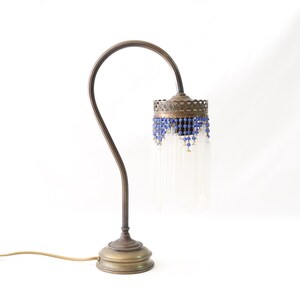 K&ouml;nnte beinhalten: Eine Tischlampe aus Messing mit einem gebogenen Arm und einem blauen und wei&szlig;en Perlenschatten.