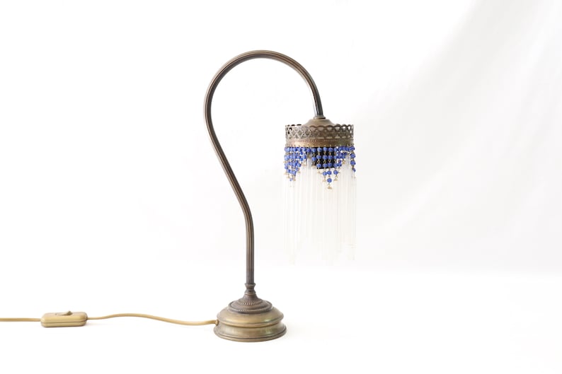 K&ouml;nnte beinhalten: Eine Tischlampe aus Messing mit einem gebogenen Arm und einem blauen und wei&szlig;en Perlenschatten.