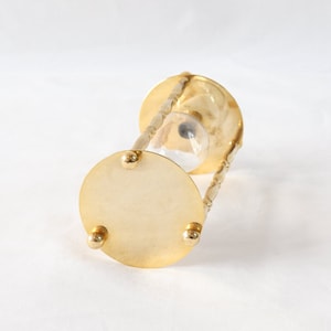 Pu&ograve; includere: Una clessidra color oro con un centro in vetro trasparente. La clessidra ha una base e una parte superiore circolari, collegate da supporti curvi e ornati. La base ha tre piccoli piedini arrotondati. La clessidra &egrave; progettata per misurare il tempo.