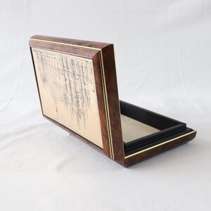 May include: A wooden box with a gold-colored interior and a black lining. The lid is open and features a decorative design on the inside.