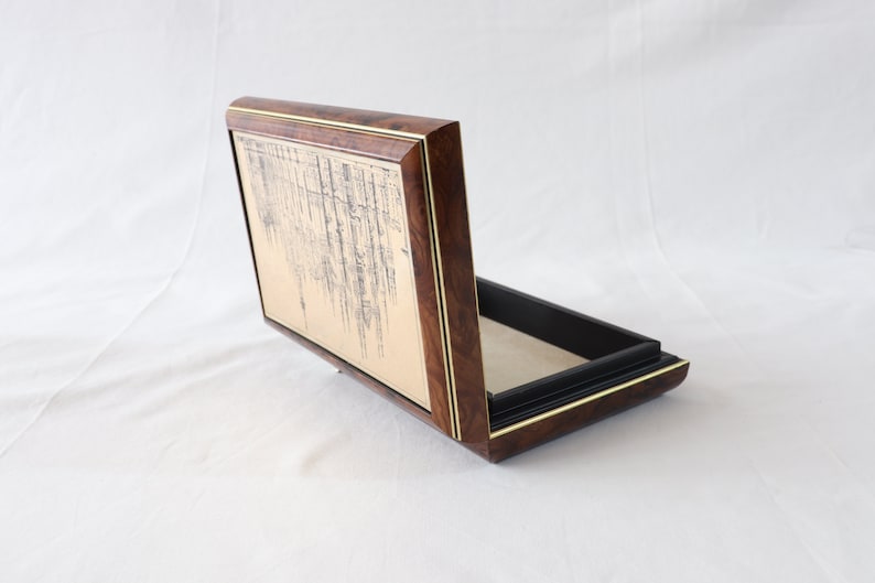 May include: A wooden box with a gold-colored interior and a black lining. The lid is open and features a decorative design on the inside.