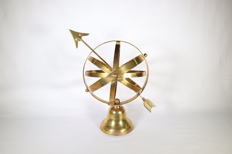 May include: A gold-toned metal sculpture of a sphere with a compass arrow on a bell-shaped base.