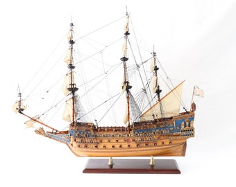 May include: A detailed wooden model of a historic sailing ship with intricate carvings and a blue and gold paint scheme. The ship has multiple masts and sails, and is displayed on a wooden base.