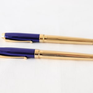 May include: Two gold and blue pens with a ribbed design. The pens have a gold clip and a blue barrel.