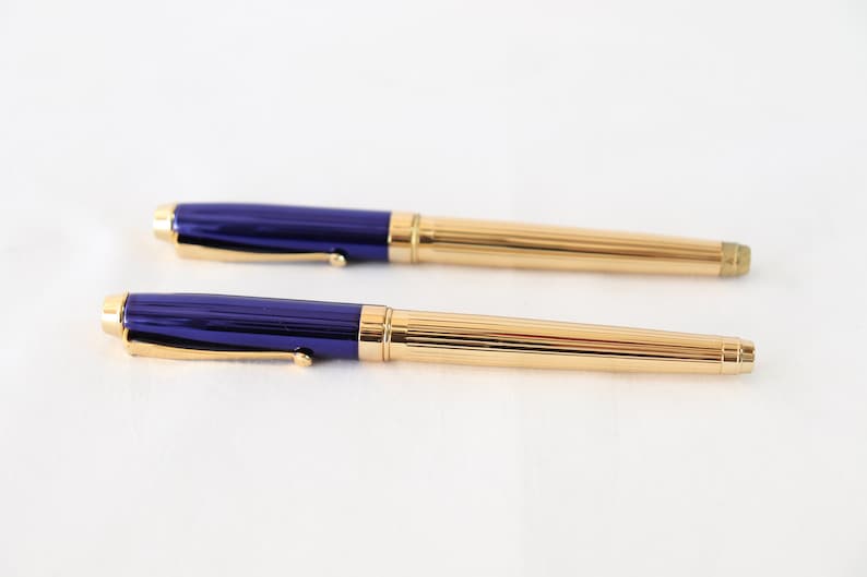 May include: Two gold and blue pens with a ribbed design. The pens have a gold clip and a blue barrel.