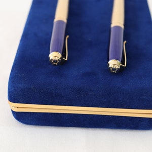 May include: A blue velvet pen case with gold trim, containing two gold and blue pens.