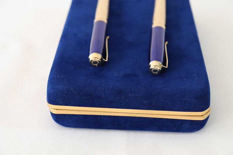 May include: A blue velvet pen case with gold trim, containing two gold and blue pens.