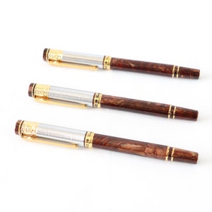 May include: Three brown and silver pens with gold accents. The pens have a wood-like finish and are arranged in a row.