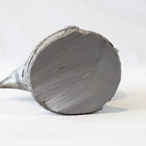 May include: A ceramic bird figurine with a grey glaze. The bird is perched on a base and has a long, pointed beak. The base of the figurine is flat and circular.