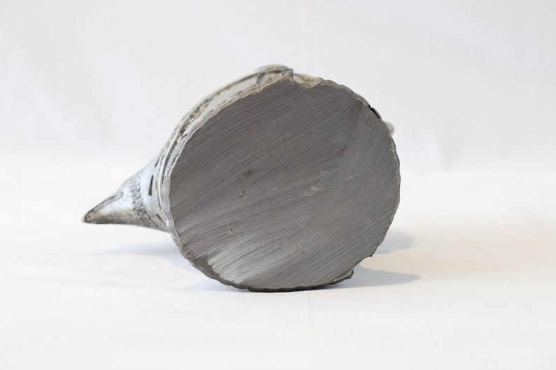 May include: A ceramic bird figurine with a grey glaze. The bird is perched on a base and has a long, pointed beak. The base of the figurine is flat and circular.