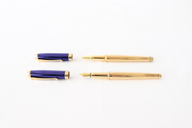 May include: A set of two pens, one with a blue barrel and a gold cap and the other with a gold barrel and a gold cap.