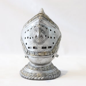 May include: A silver knight's helmet with intricate details and a gold trim. The helmet is on a white background.