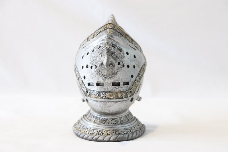 May include: A silver knight's helmet with intricate details and a gold trim. The helmet is on a white background.