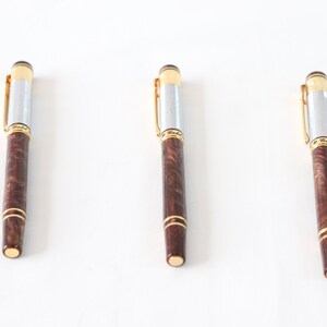 May include: Three brown and silver pens with gold accents. The pens have a wood grain pattern and are arranged in a row on a white surface.