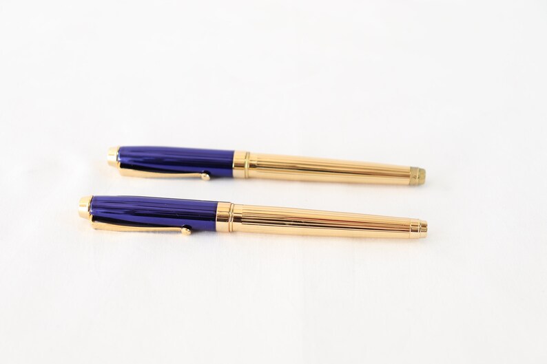 May include: A set of two gold and blue pens. The pens have a gold trim and a blue barrel.