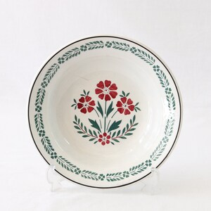 Könnte beinhalten: Weiße Keramikschüssel mit einem grünen und roten Blumendesign. Die Schüssel hat einen schwarzen Rand und ein grünes und weißes Blumenmuster am Rand.