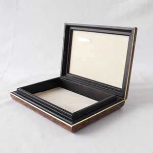 May include: A wooden box with a black interior and a gold trim. The box is open and the lid is propped up.
