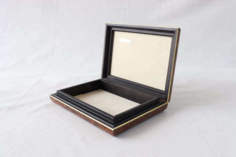 May include: A wooden box with a black interior and a gold trim. The box is open and the lid is propped up.