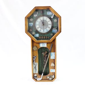 May include: Wooden golf-themed wall clock with a light brown octagonal frame. The clock face has Roman numerals and is surrounded by golf balls and other golf-related items. The lower section has a golf club and the text "BORN TO GOLF!"