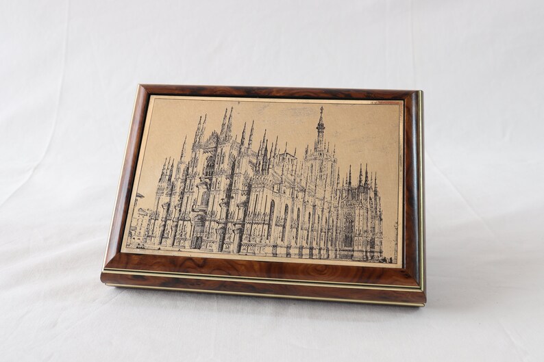 May include: A wooden box with a gold-toned metal inlay featuring a black and white line drawing of a cathedral.