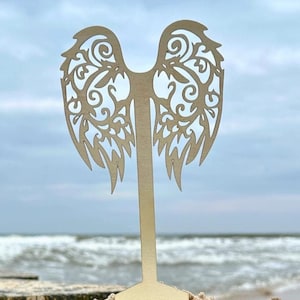 Può includere: Un supporto decorativo in legno con un design a forma di ali d'angelo ritagliate. Il supporto è in legno marrone chiaro e ha una base semplice. Le ali sono intricate e dettagliate, con un delicato motivo floreale.