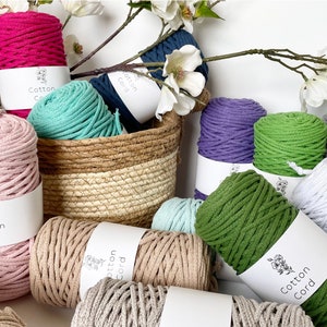 Puede incluir: Una variedad de cordones de algodón en diferentes colores, incluyendo rosa, verde, blanco, gris y azul. Los cordones están dispuestos en una cesta y sobre una superficie blanca. La etiqueta en los cordones dice "Cordón de algodón".