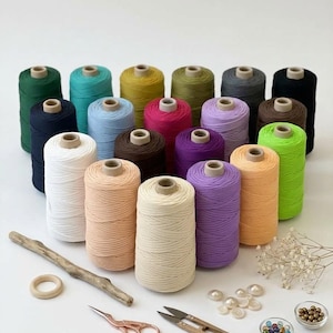 Peut inclure: Une collection de vingt et une bobines de cordon en coton coloré disposées en triangle, accompagnées d'un anneau en bois, d'un morceau de bois flotté, de ciseaux en or rose, d'un coupe-fil en bois, de boutons blancs et deux bols de perles.