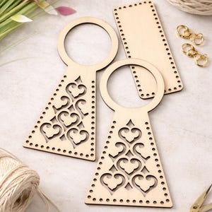 Op de afbeelding: Houten knutselbenodigdheden, waaronder twee decoratieve tasbodems met hartuitsparingen, een rechthoekig stuk, goudkleurige sluitingen en een bol touw. Een gouden schaar en een boeket bloemen zijn ook aanwezig.