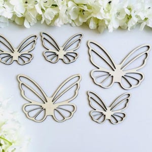 Op de afbeelding: Vijf houten vlinder vormen in verschillende maten. De vlinders zijn uit hout gesneden en hebben een natuurlijke houtkleur.