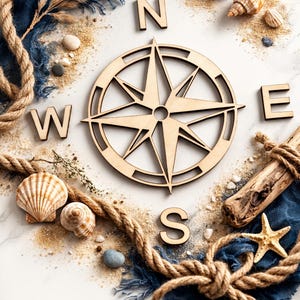 May include: A wooden compass rose with the letters N, E, S, and W, surrounded by seashells, sand, rope, and driftwood on a white surface. A starfish and blue fabric add to the nautical theme.
