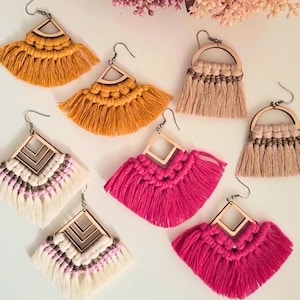 Può includere: Una collezione di orecchini in macramè fatti a mano in vari colori. Gli orecchini presentano forme geometriche in legno e dettagli con frange. I colori includono giallo senape, rosa acceso e tonalità neutre. Gli orecchini sono progettati con ganci argentati.