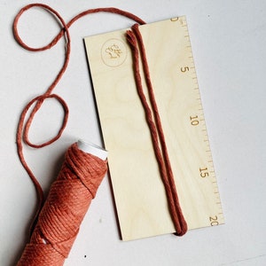 May include: A wooden board with a ruler marked in centimeters, a spool of brown cord, and a length of brown cord wrapped around the board. The board has the text "Etsy Find" printed on it.