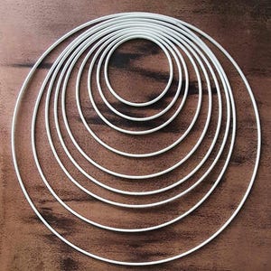 Puede incluir: Un conjunto de ocho aros de metal blanco de diferentes tamaños, dispuestos en un patrón concéntrico. Los aros son todos circulares y tienen un acabado liso y pulido.