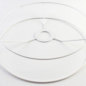 Puede incluir: Estructura de pantalla de l&aacute;mpara de metal blanco con forma circular y un anillo interior m&aacute;s peque&ntilde;o. La estructura tiene un soporte central con cinco radios.