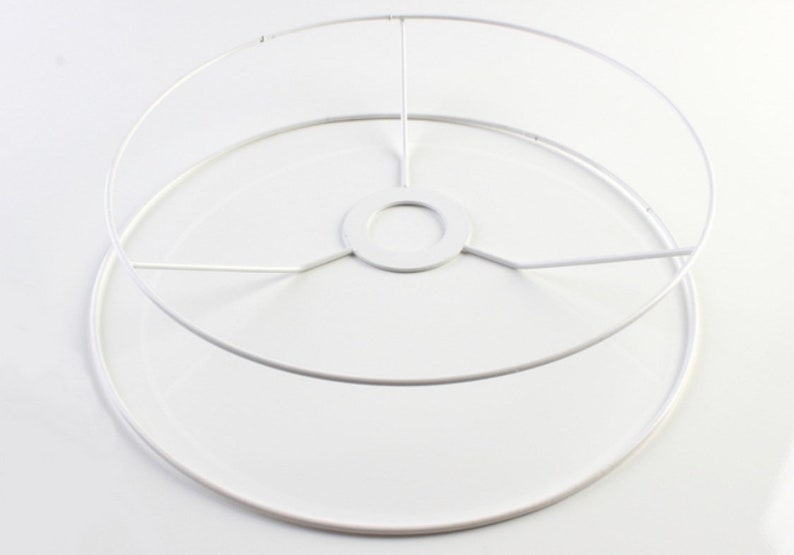 Puede incluir: Estructura de pantalla de l&aacute;mpara de metal blanco con forma circular y un anillo interior m&aacute;s peque&ntilde;o. La estructura tiene un soporte central con cinco radios.