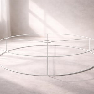 May include: A white metal lampshade frame. The frame is circular with a series of horizontal and vertical supports. The structure is designed to hold fabric or other materials to create a lampshade. The frame is set against a neutral background.
