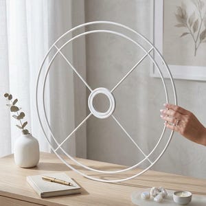 Peut inclure: Un cadre circulaire en métal blanc composé de deux anneaux concentriques reliés par quatre rayons fins qui se rejoignent au niveau d'un moyeu central. La structure est légère et ouverte, avec une esthétique géométrique et une finition mate.