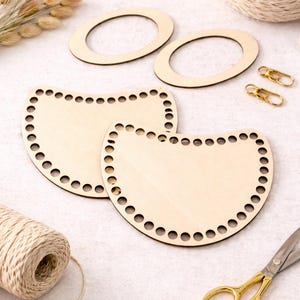 May include: Wooden craft supplies including two oval-shaped bases, two half-circle bases with holes, gold-colored clasps, scissors, and twine. The items are arranged on a light-colored surface, suggesting a crafting theme.