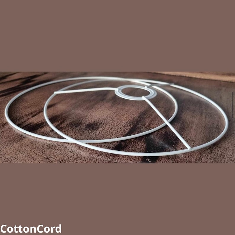 Puede incluir: Dos anillos de pantalla de l&aacute;mpara de metal blanco, uno dentro del otro, sobre una superficie de madera marr&oacute;n.