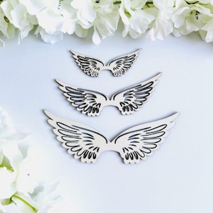 Op de afbeelding: Drie houten engelenvleugels in verschillende maten, met een witte achtergrond. De vleugels zijn ingewikkeld gesneden met een gedetailleerd ontwerp.