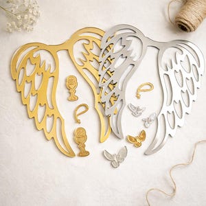 Könnte beinhalten: Gold- und silberfarbene Engelsflügel-Ornamente und -Anhänger. Die Flügel sind mit aufwendigen Details ausgeschnitten. Ebenfalls enthalten sind goldene Kelche, kleine goldene und silberne Tauben sowie goldene tropfenförmige Anhänger.